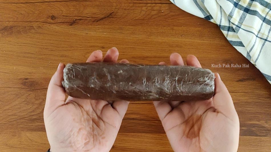 Shaped cookie dough log wrapped in cling wrap.