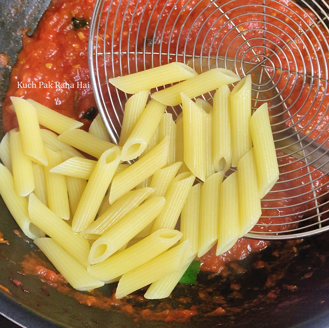 Adding boiled pasta to red sauce.