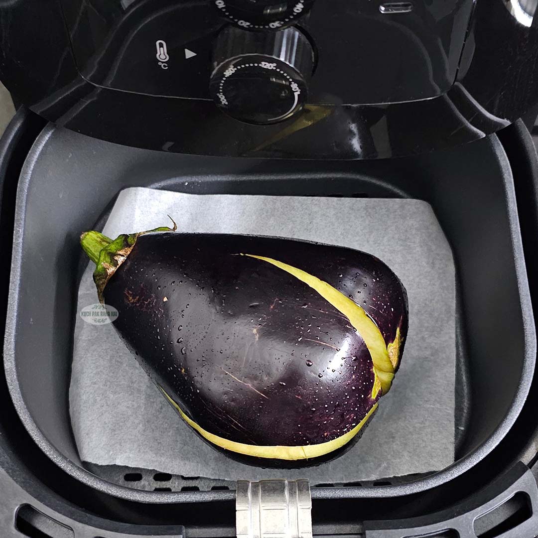Placing whole eggplant in airfryer basket.