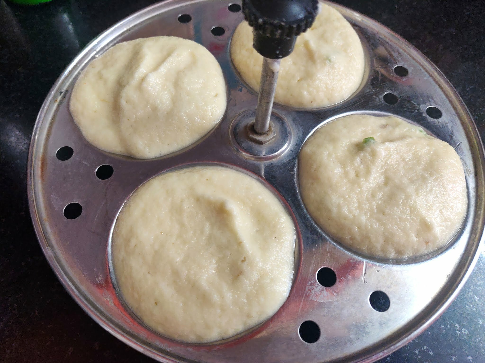 Pouring moong dal idli batter on idli plate.