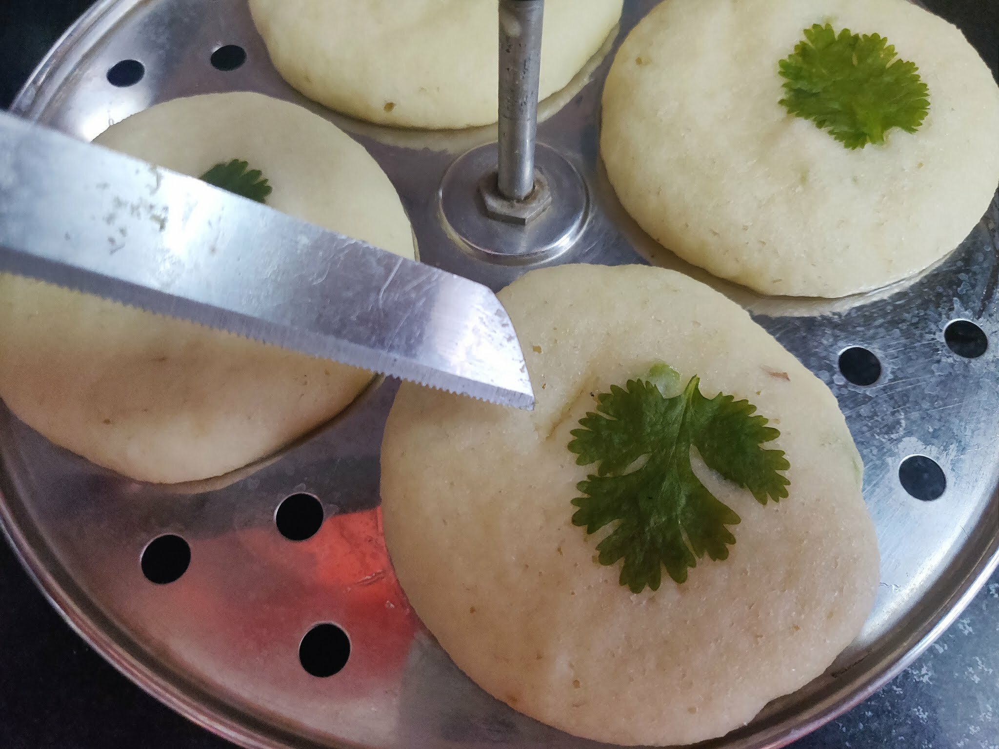 Checking centre if idli with knife for doneness.