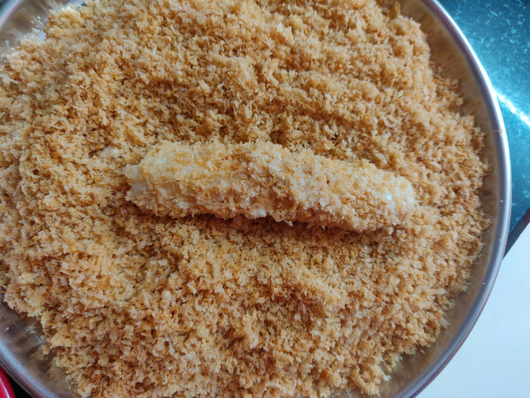 Rolling the baby corns in bread crumbs.