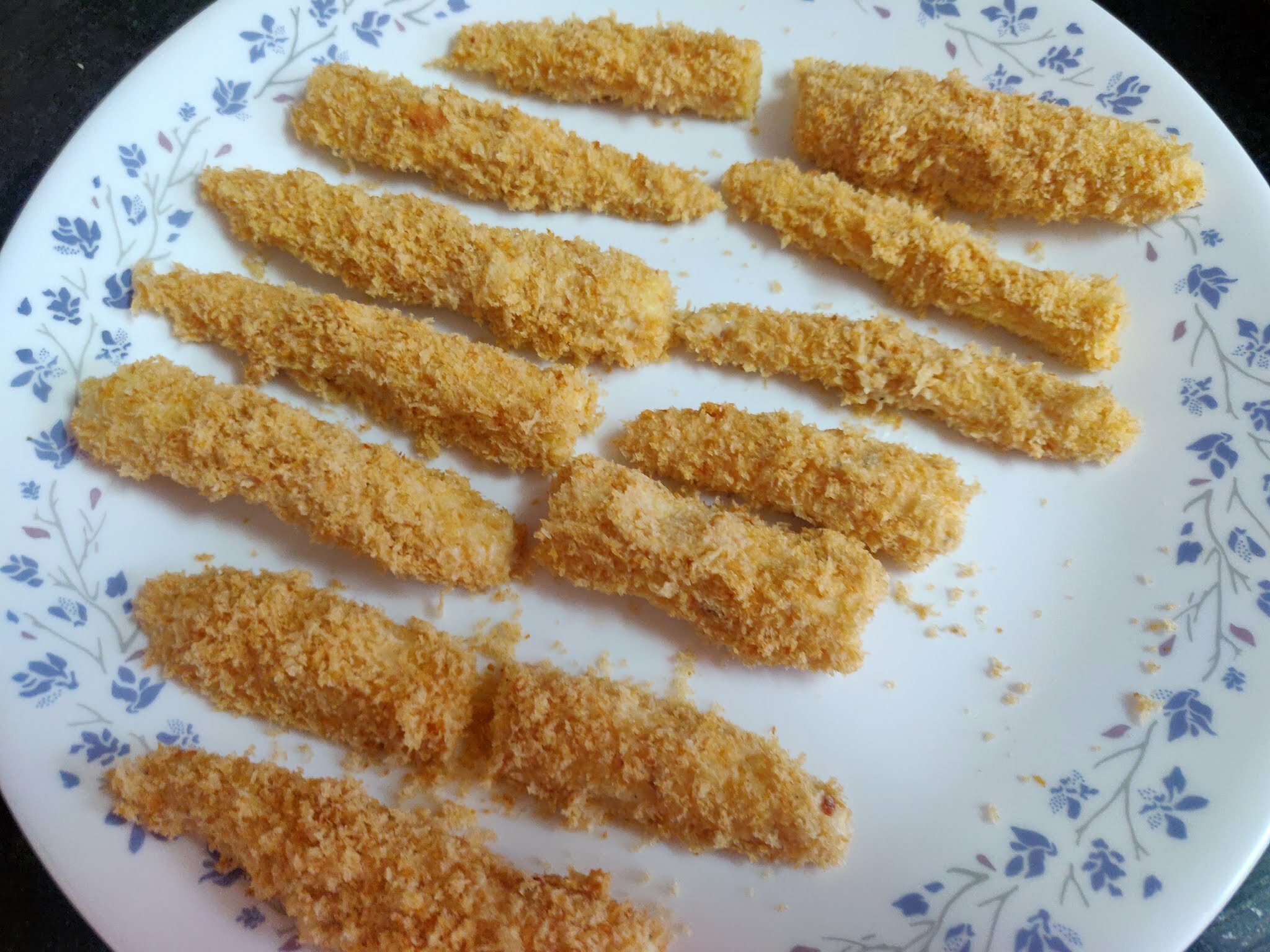 Breaded baby corns on a plate before air frying.