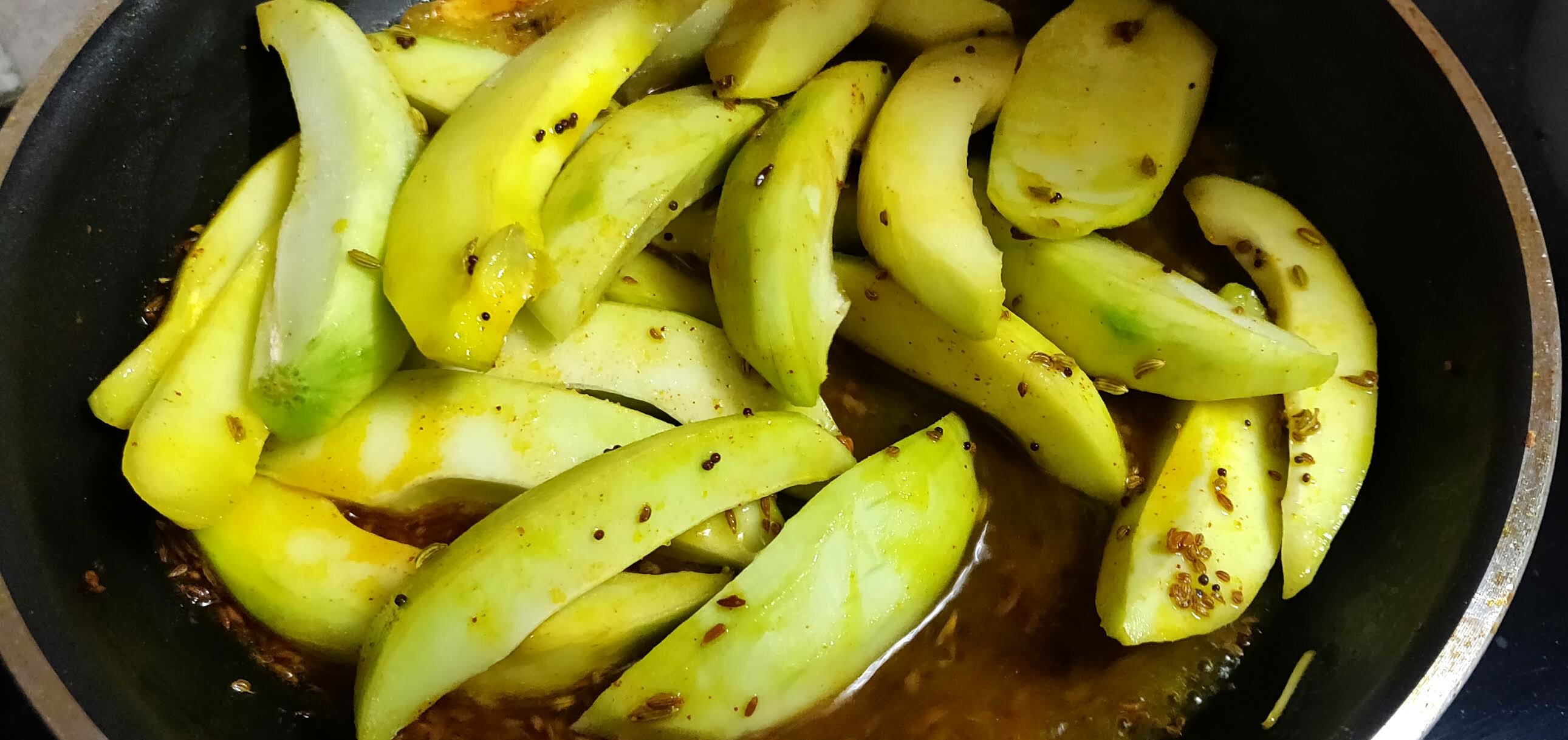 Adding sliced raw mangoes to cooked spices.