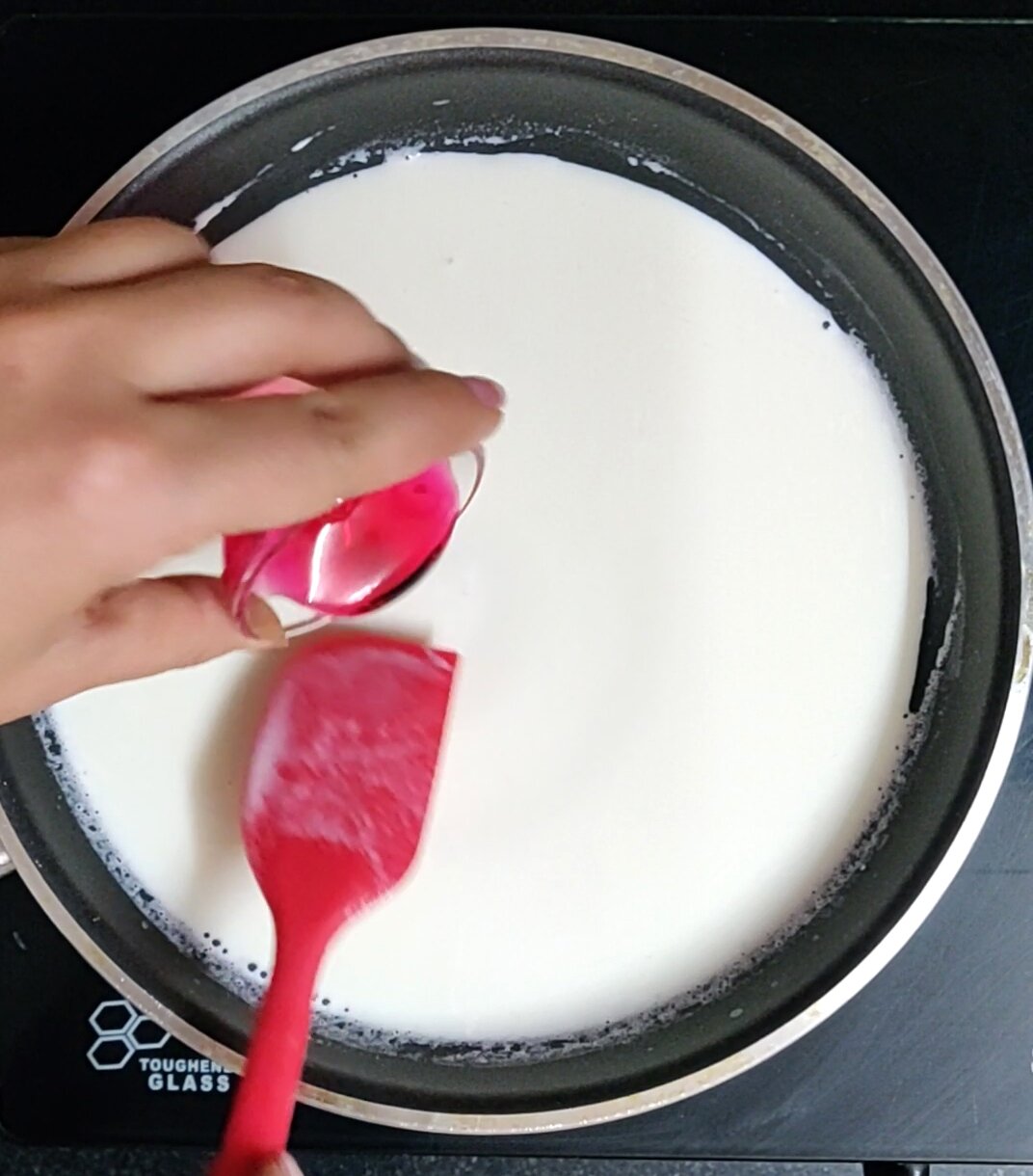Adding rose syrup to the heated milk.