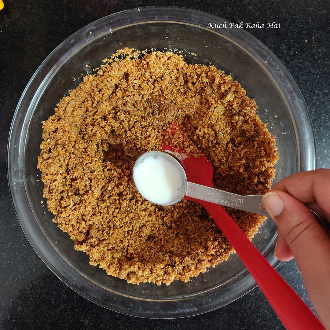 Adding spoonful of milk to oats jaggery mixture for binding.