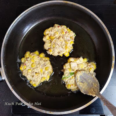 Spreading corn fritters in pan using spoon. 
