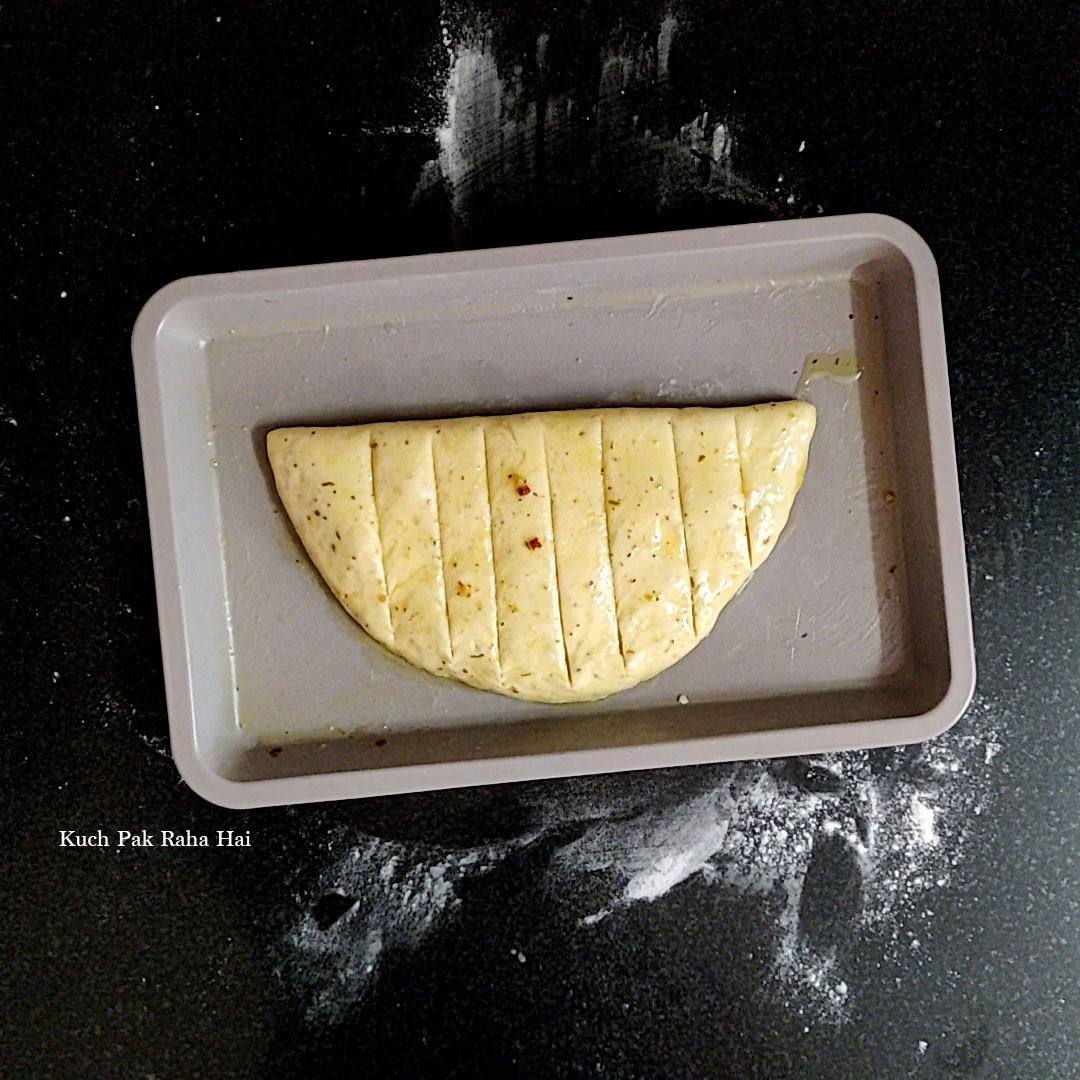 Shaped unbaked garlic bread in baking tray.