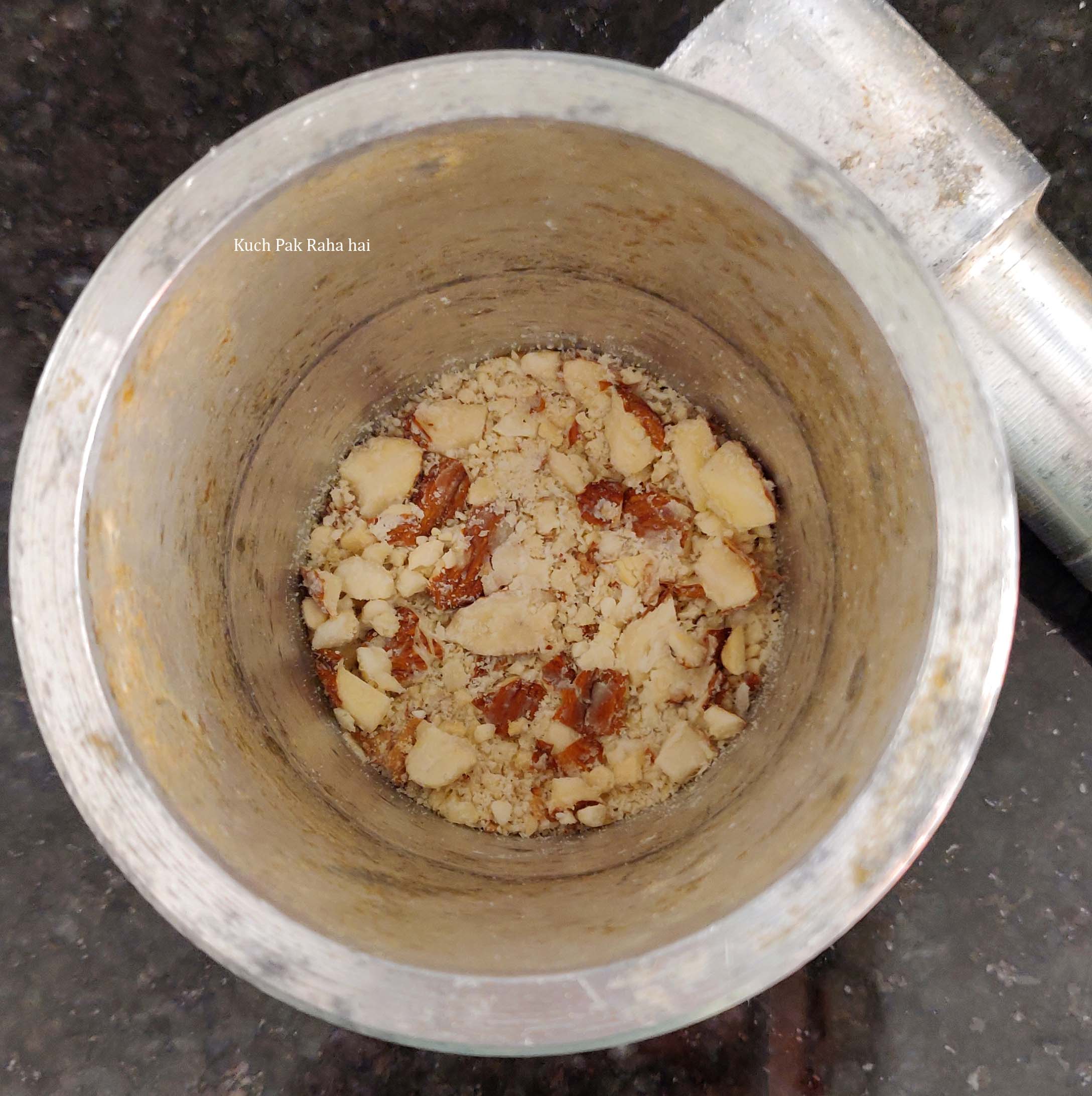 Pounding almonds cashews in mortar pestle.