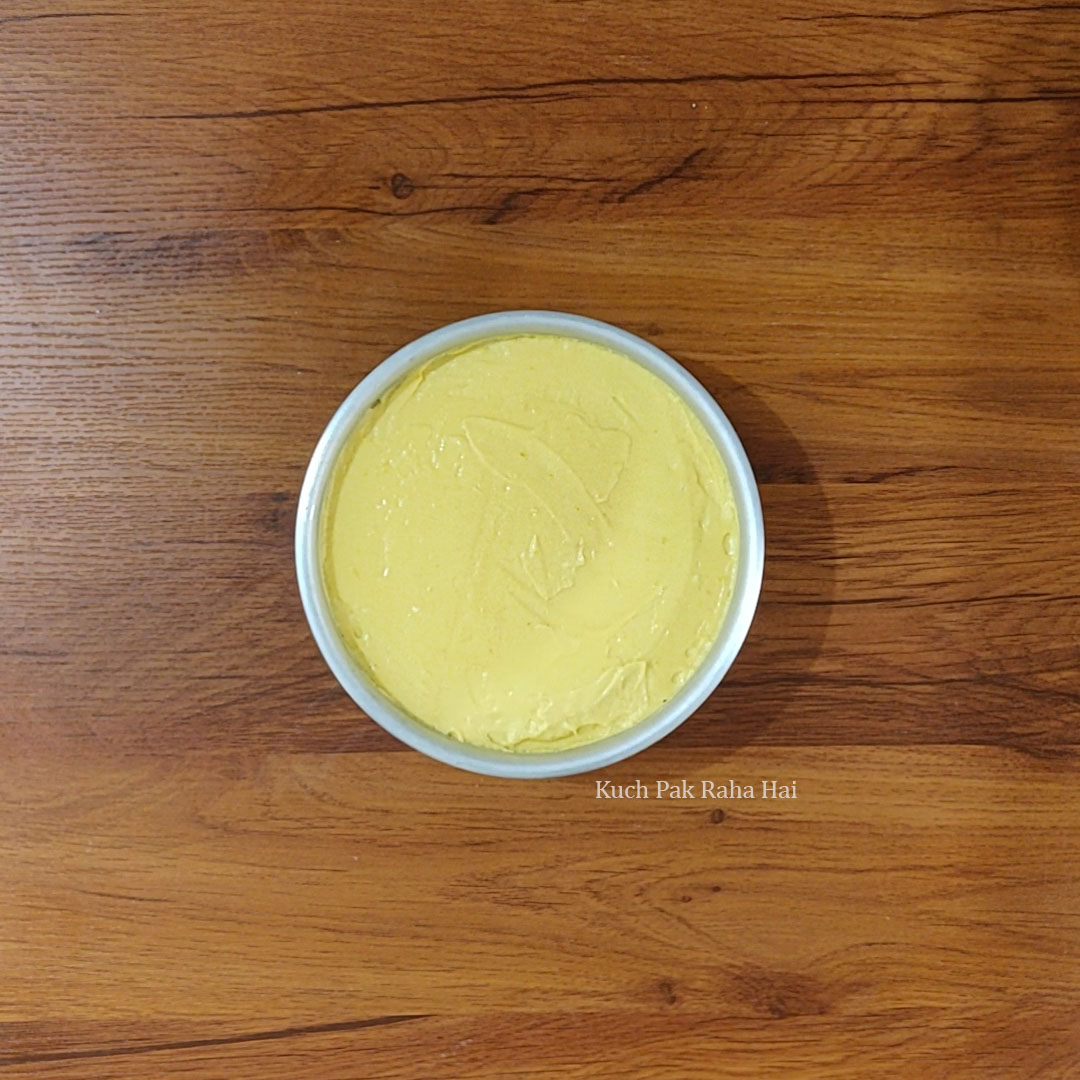 Transferring mango cheesecake filling on biscuit crust.