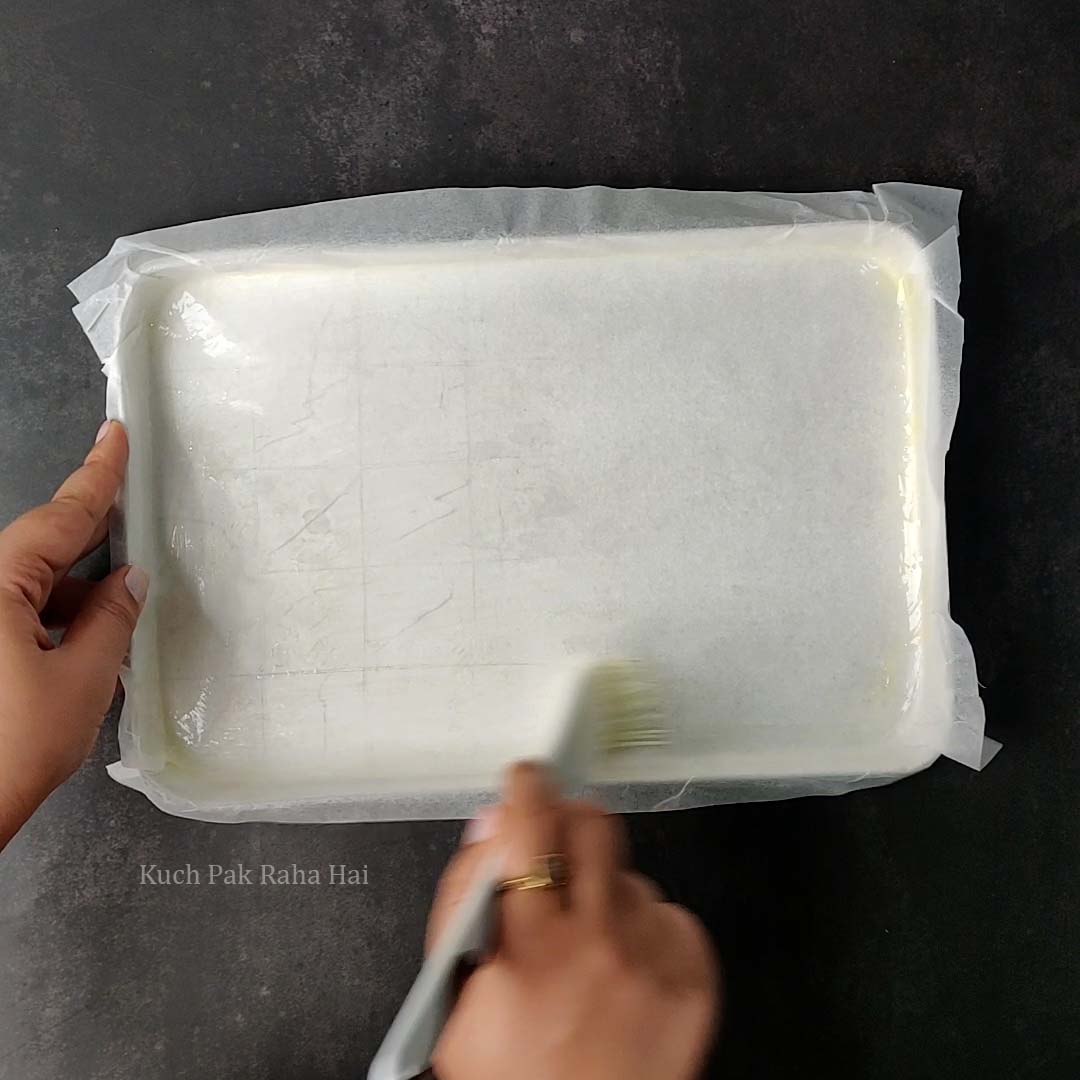 Lining barfi tray with parchment paper and brushing with ghee.