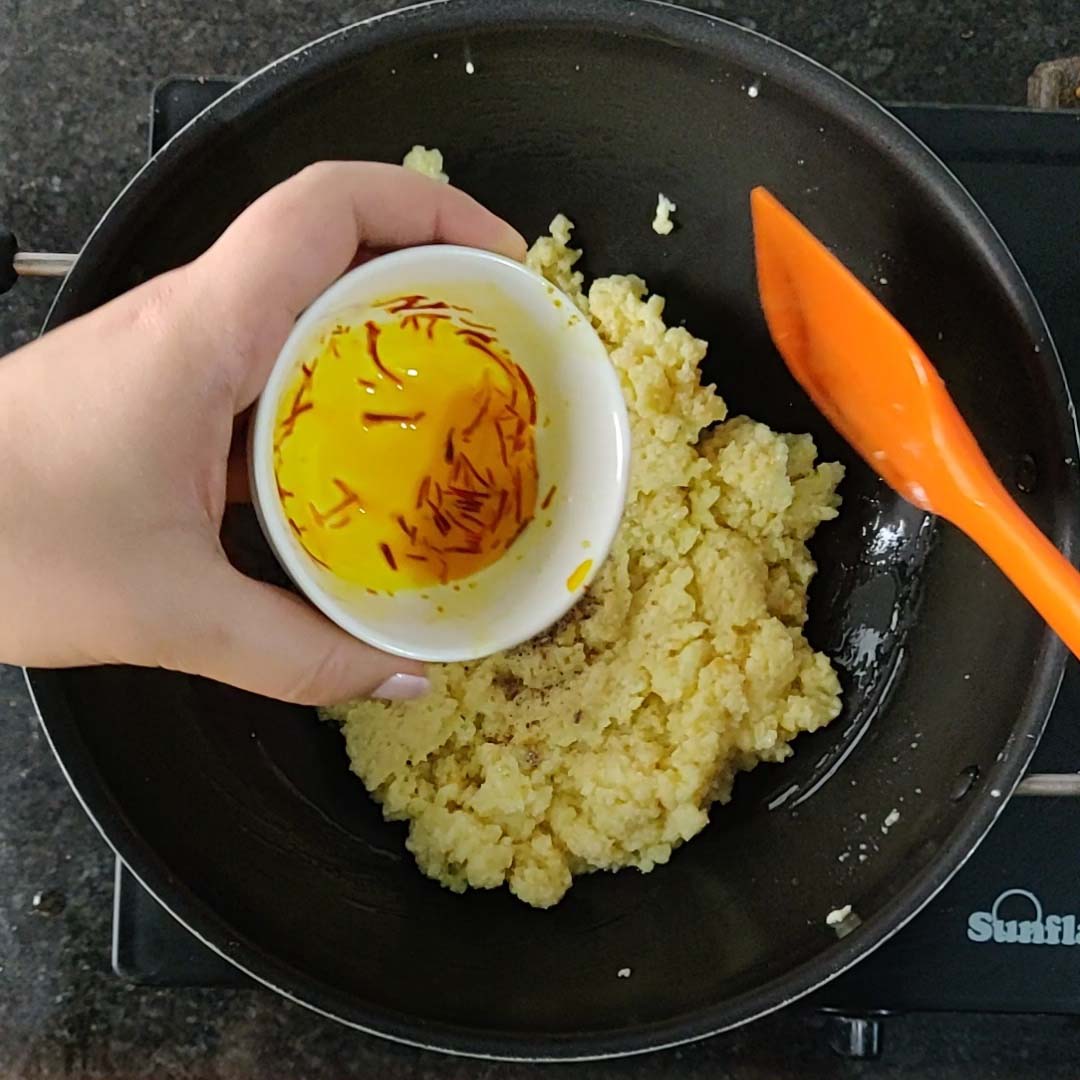 Adding sugar and saffron milk to the burfi mixture.