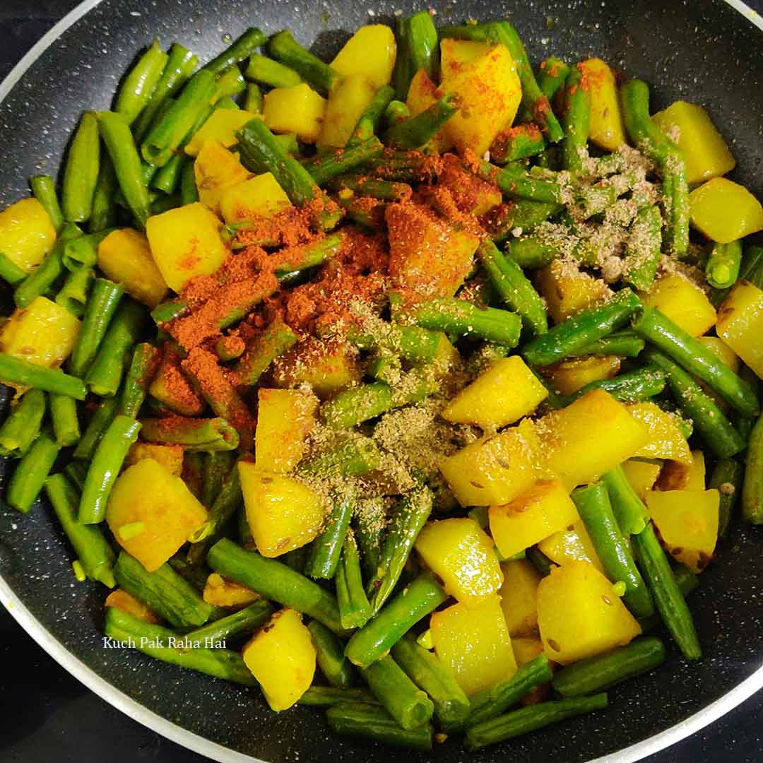 Adding spices to green beans potatoes.