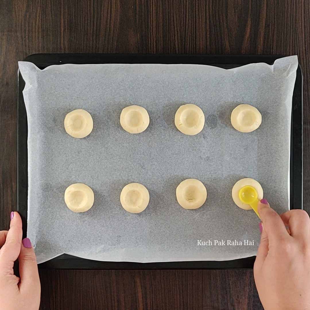 Making well in centre of cookies to fill with jam.