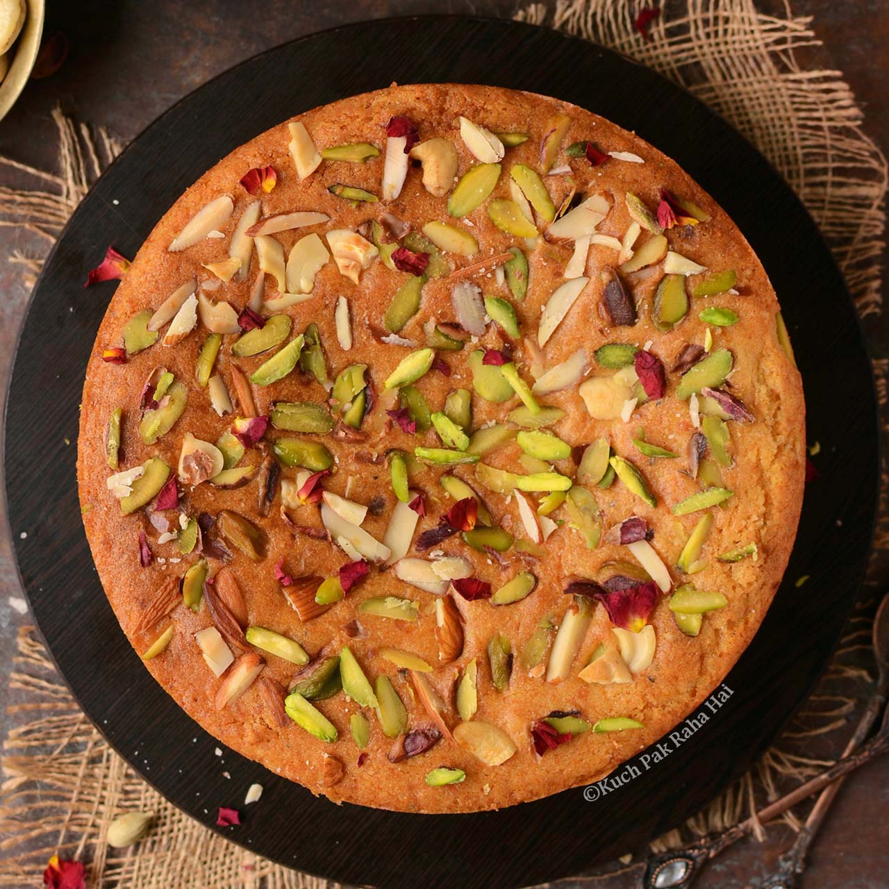 Eggless Mawa Cake with nuts served on black plate.