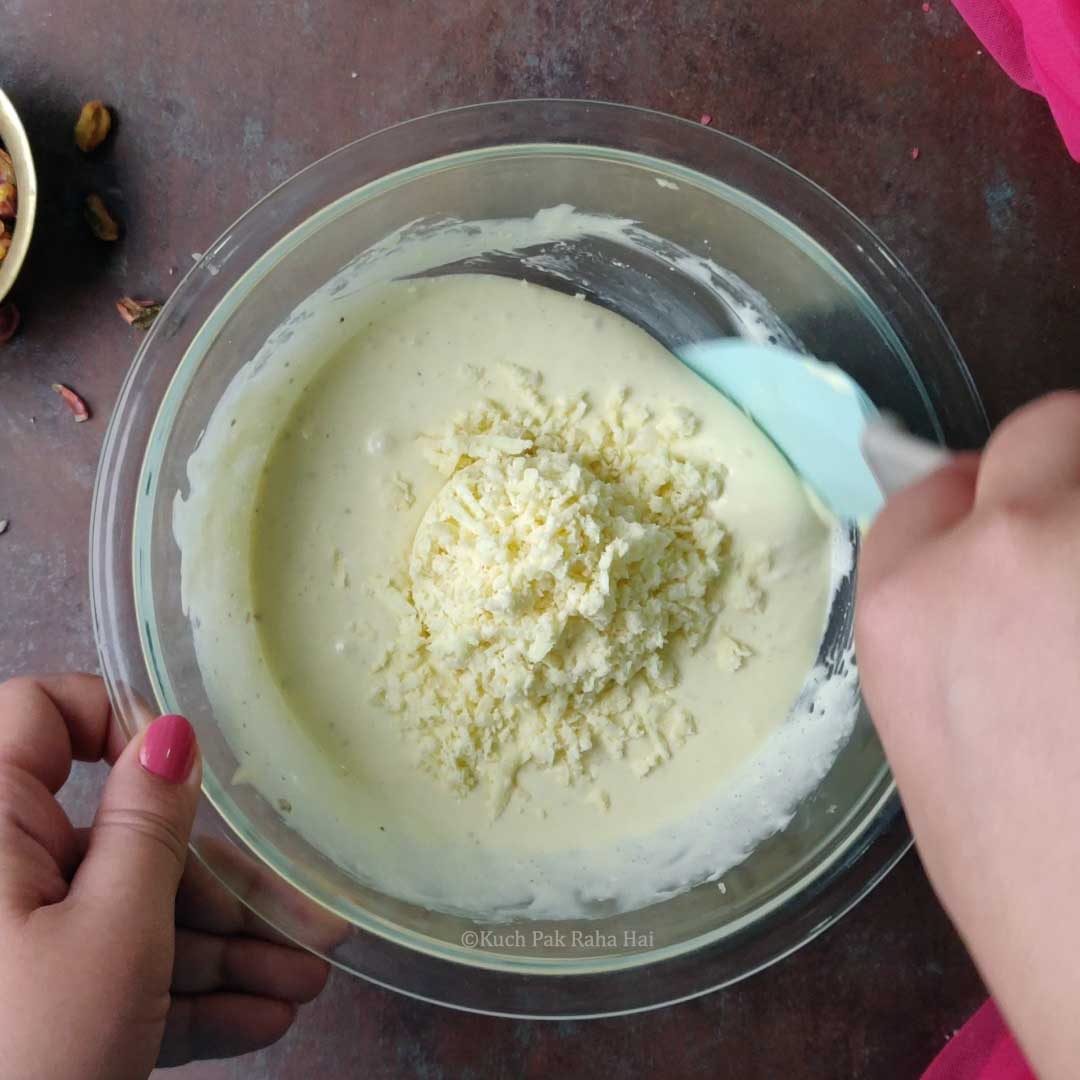 Adding grated mawa to wet ingredients.