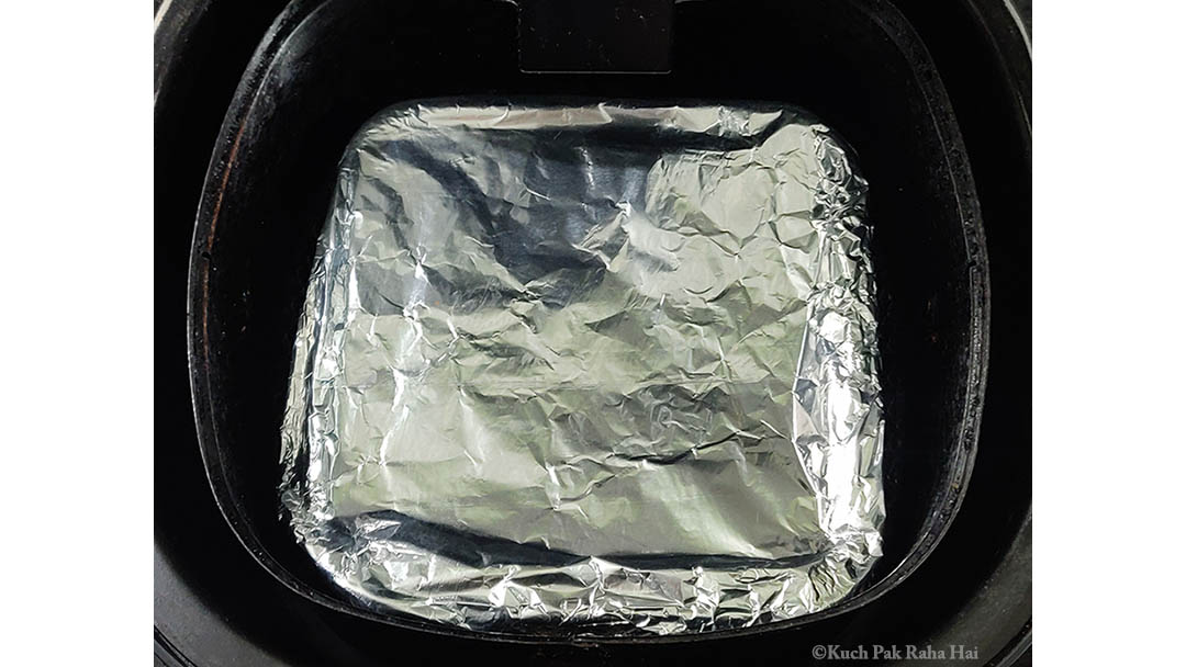 Apple filling in baking dish covered with foil in air fryer basket.
