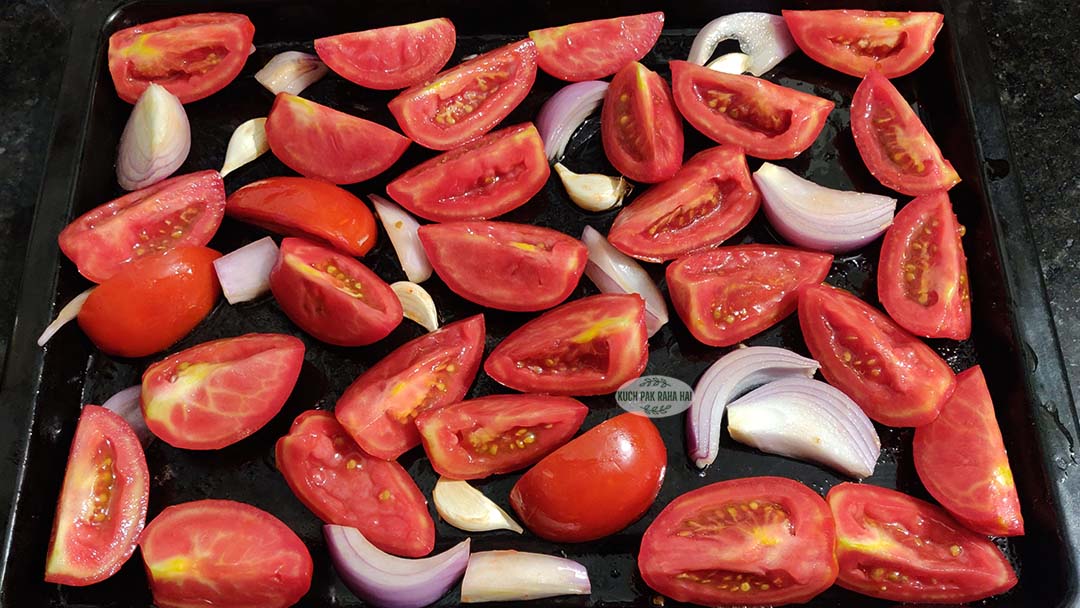 Tomatoes garlic onion on a baking tray before roasting.