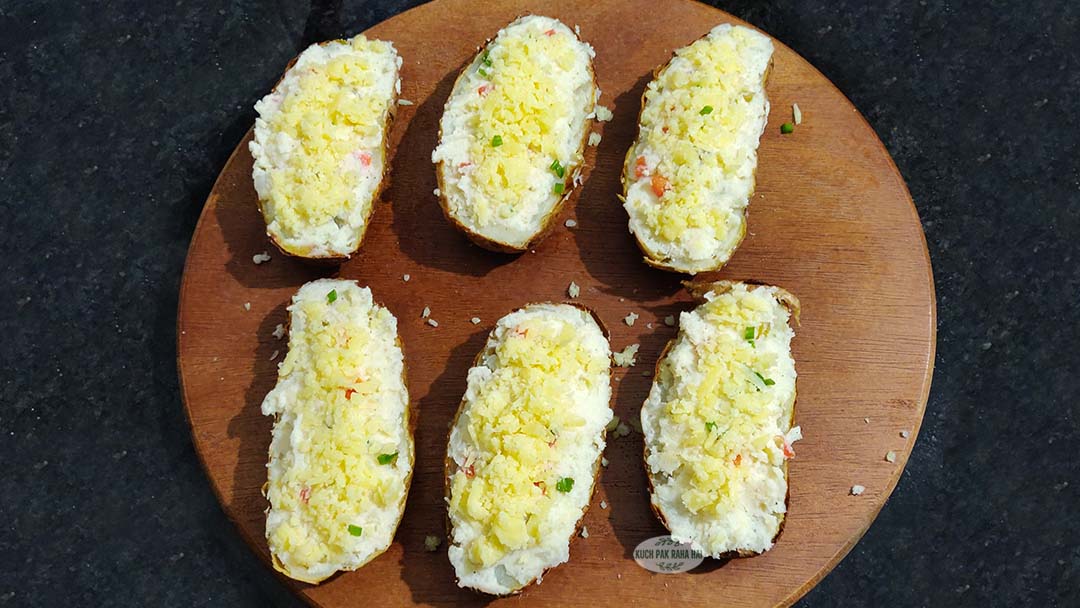 Adding cheese on top of stuffed potatoes.