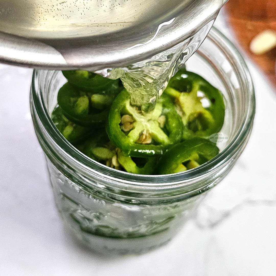 Pouring liquid brine on jalapeno and garlic.